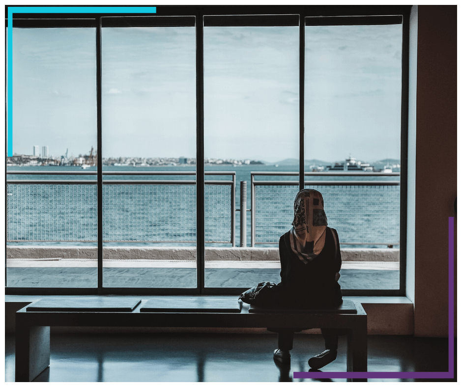 A woman sits in front of a window, watching the ocean outside