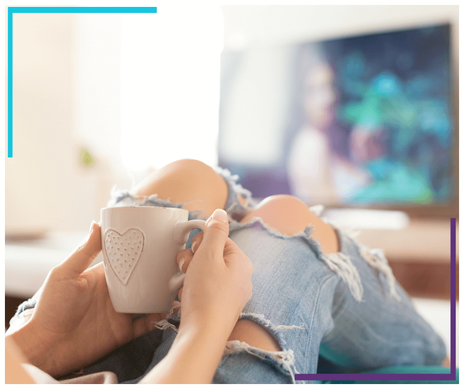 woman relaxing on the sofa at home, watching comfort tv shows and enjoying coffee